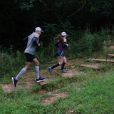 two runners on a trail in the forest, one wearing compression bracing socks in grey, one in black | OS1st