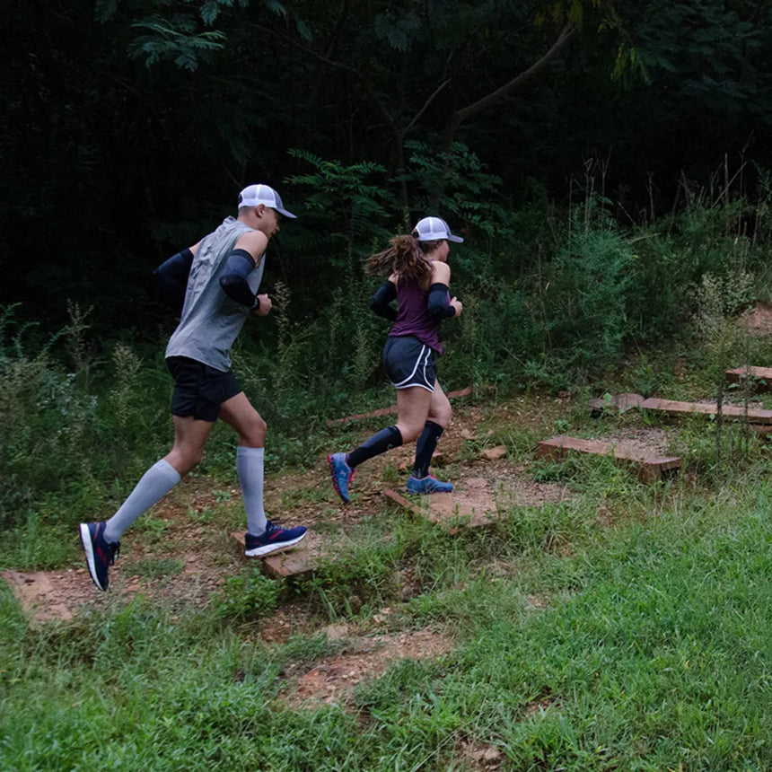 two runners on a trail in the forest, one wearing compression bracing socks in grey, one in black | OS1st