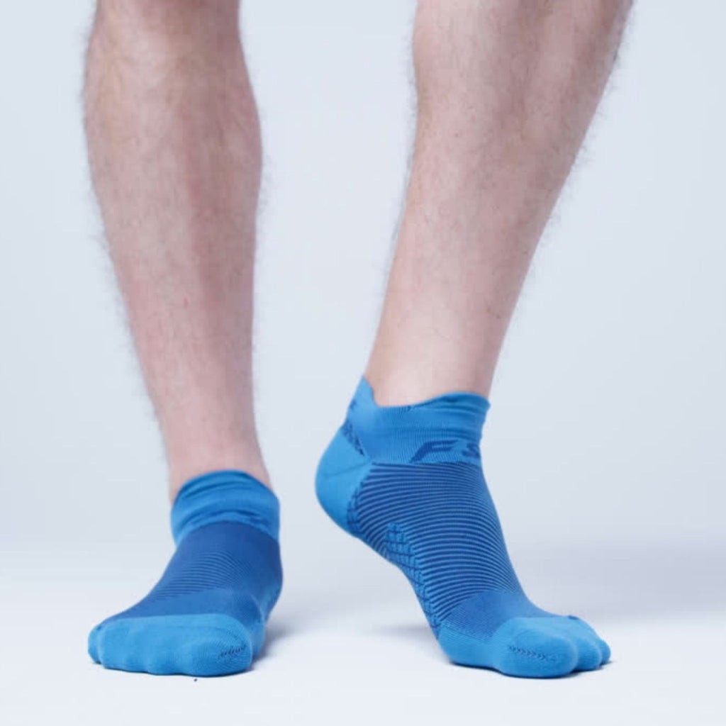 A man wearing our royal blue plantar fasciitis socks lifting his right foot up to show the targeted arch compression