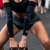 A woman working out and lifting a weight who is wearing two AS6 performance arm sleeves | OS1st