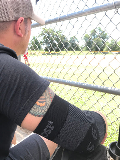 man watching a sporting event while wearing the ES6 elbow bracing sleeve | OS1st